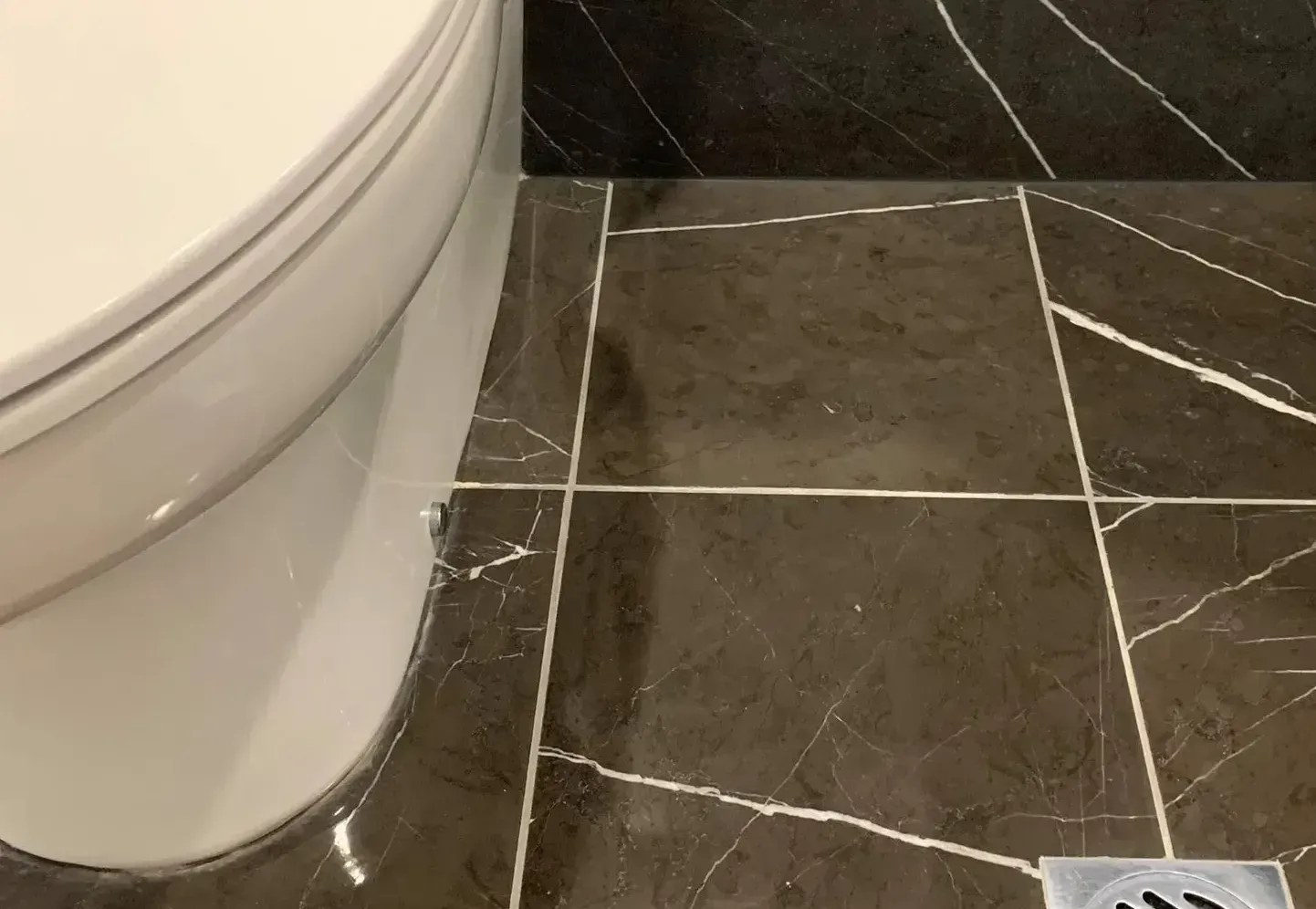 A toilet is sitting on a tiled floor next to a drain