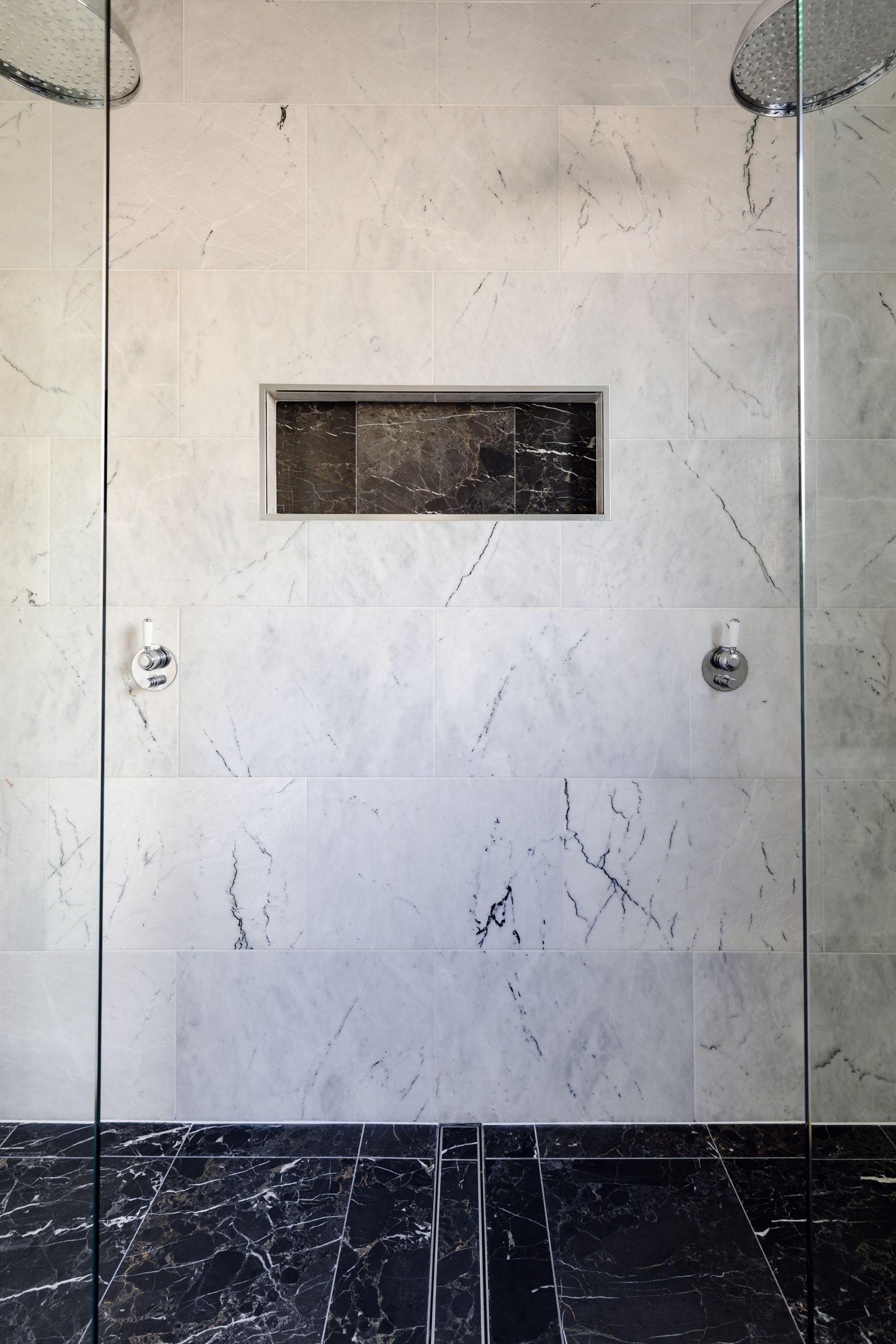 A shower stall with marble tiles and a black floor.
