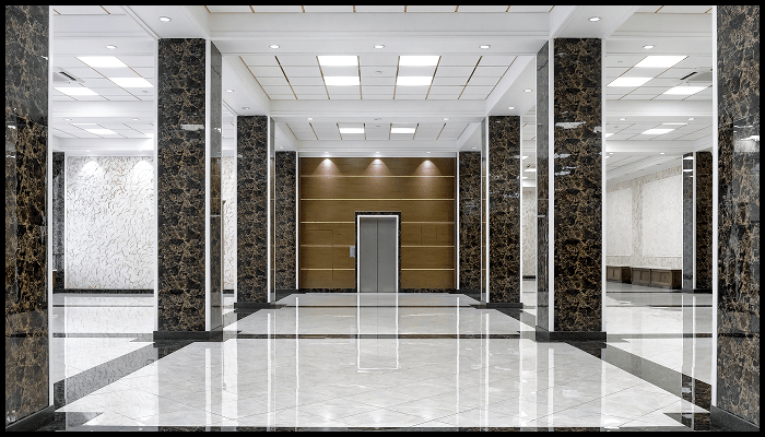 A large empty lobby with marble floors and columns and an elevator.