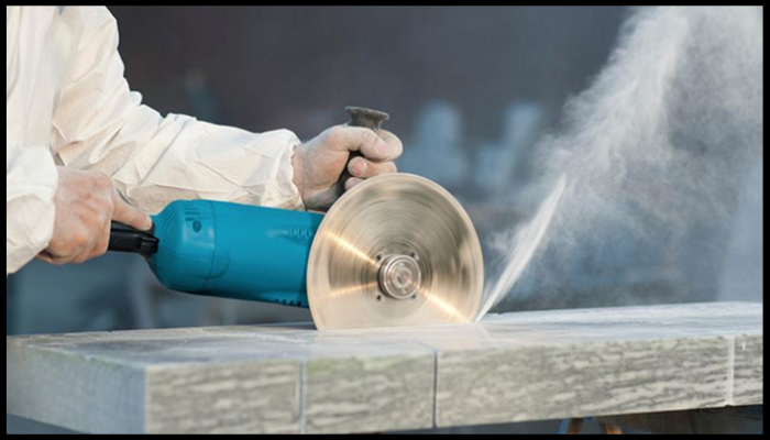 Worker cutting engineered stone with an electric saw, creating a visible cloud of silica dust, which highlights the risks when benchtops are disturbed