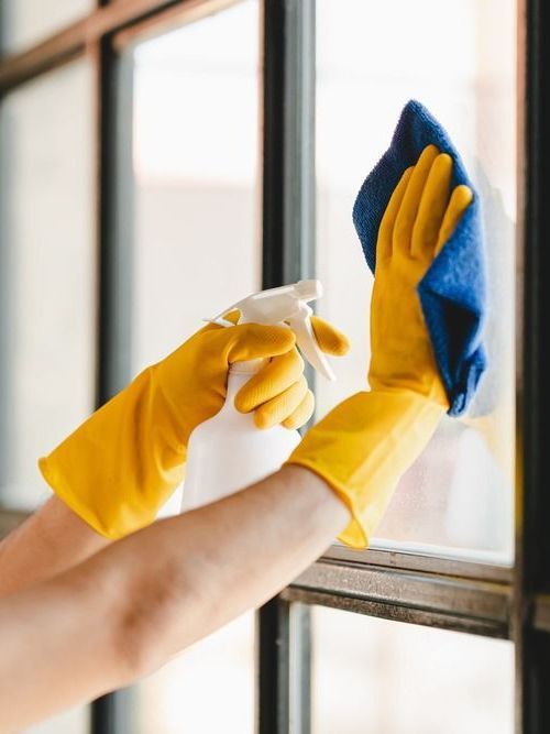 A person wearing yellow gloves is cleaning a window with a spray bottle and a cloth.