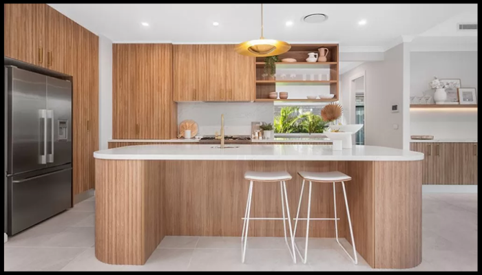 A kitchen with wooden cabinets , stools , a refrigerator , and a large island.