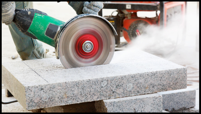 Worker cutting granite with an angle grinder, producing visible silica dust that highlights the health risks of inhaling fine particles.