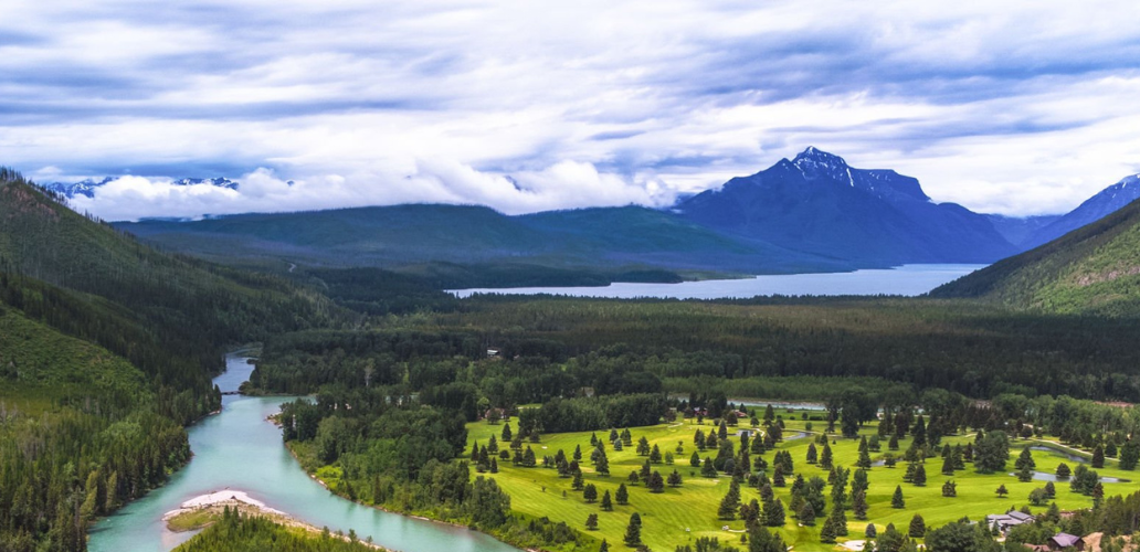 Scenic aerial view of the Flathead River with forested mountains and open green spaces near Whitefish, Montana.
