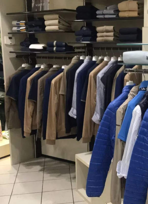 Espositore di un negozio di abbigliamento con giacche e camicie di vari colori.
