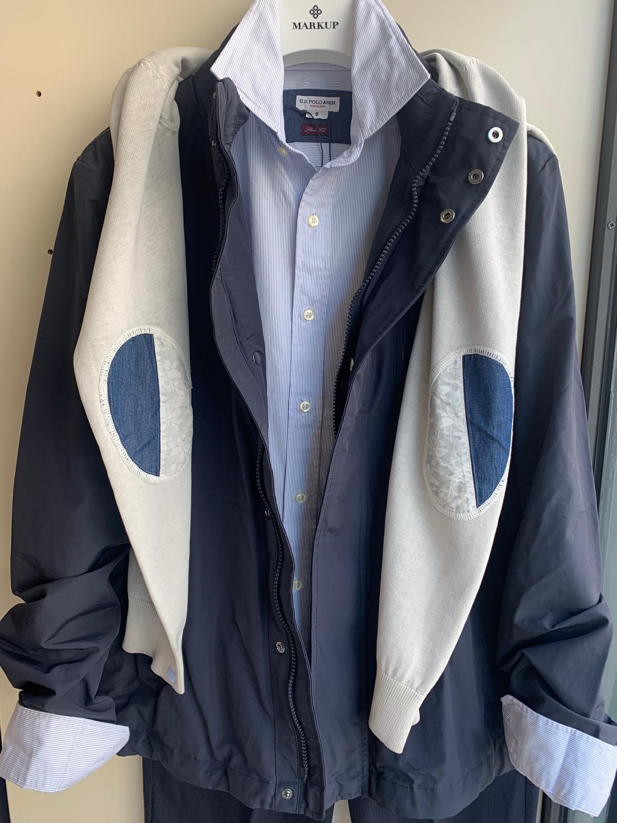 Tre manichini in vetrina espongono vari abiti: giacche, maglioni e pantaloni nei toni del blu, del marrone e del beige.