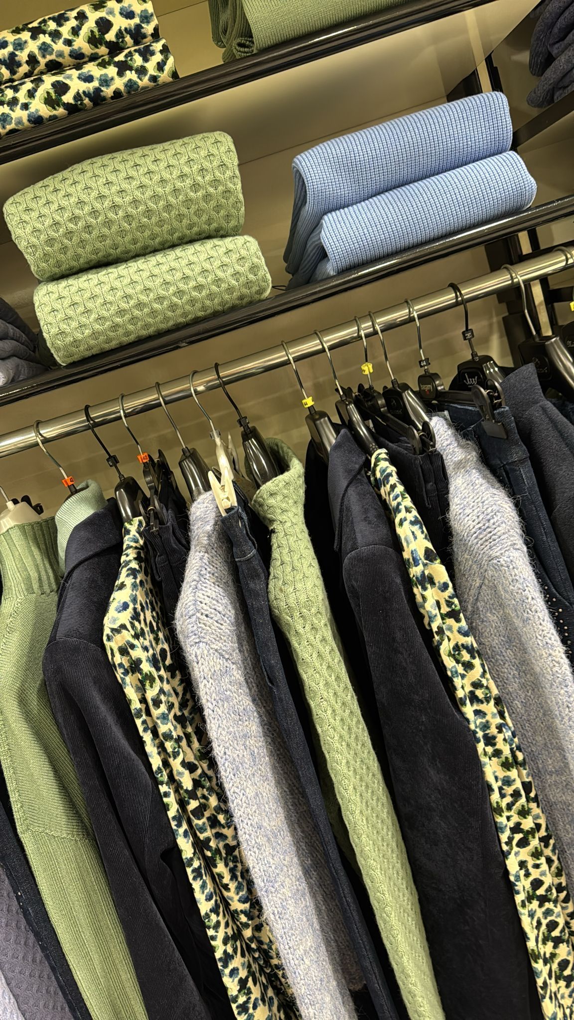 Espositore di abiti con giacche di vari colori e texture, scaffali con tessuti piegati.