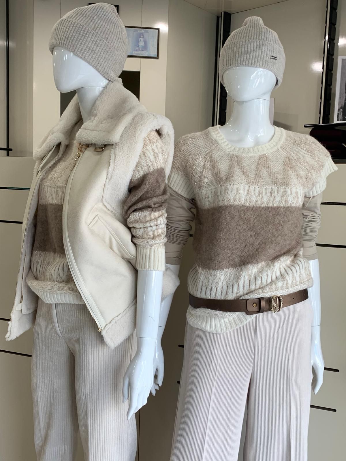 Due manichini esposti in un espositore di un negozio, indossano abiti invernali. Maglioni, gilet, cappelli e pantaloni beige e marroni.
