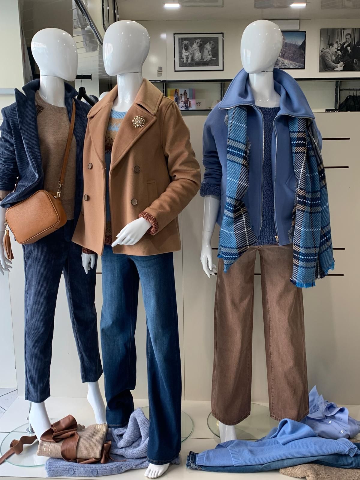 Tre manichini in vetrina espongono vari abiti: giacche, maglioni e pantaloni nei toni del blu, del marrone e del beige.