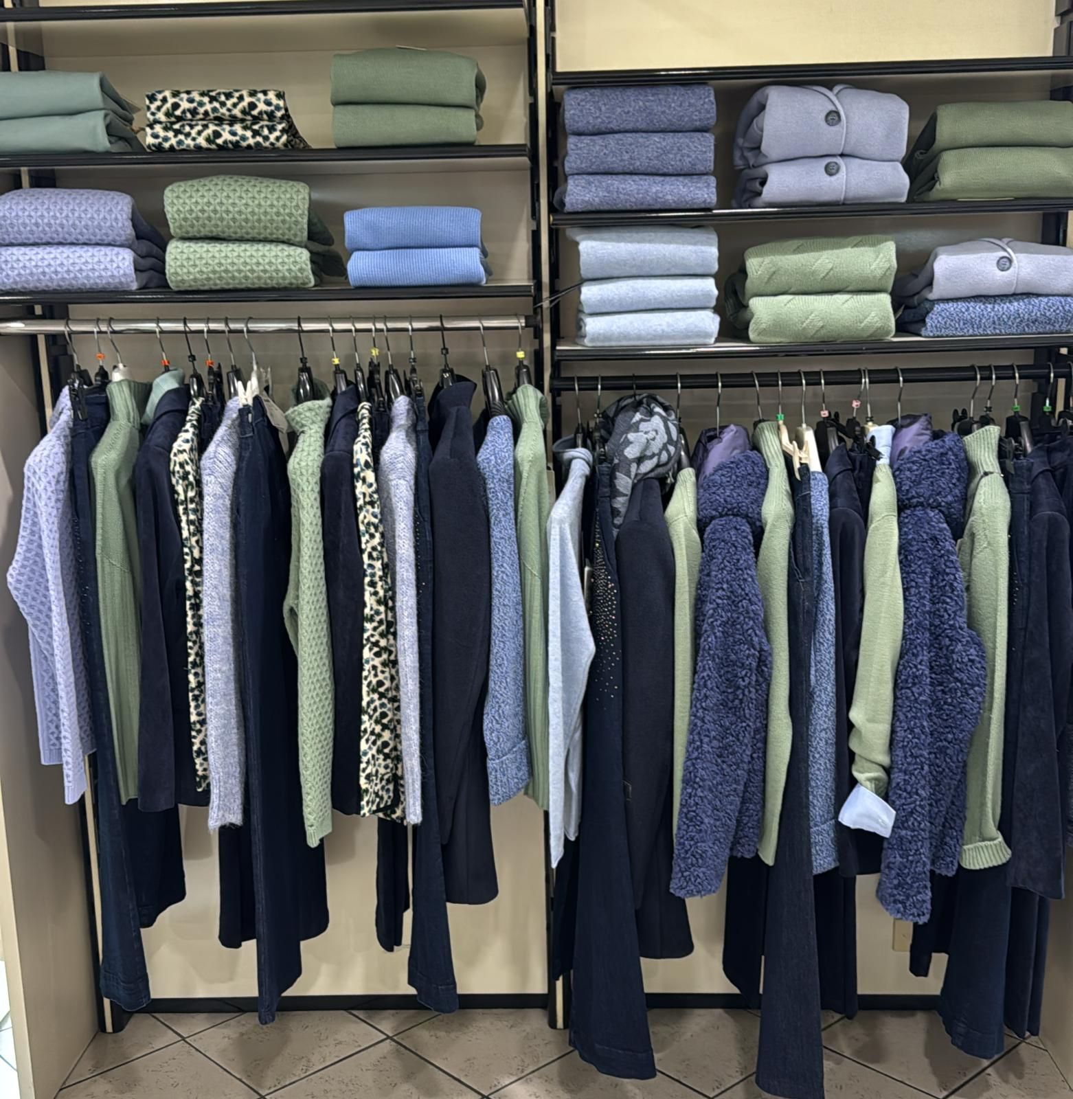 Esposizione di un negozio di abbigliamento con indumenti piegati sugli scaffali e vestiti appesi di vari colori.