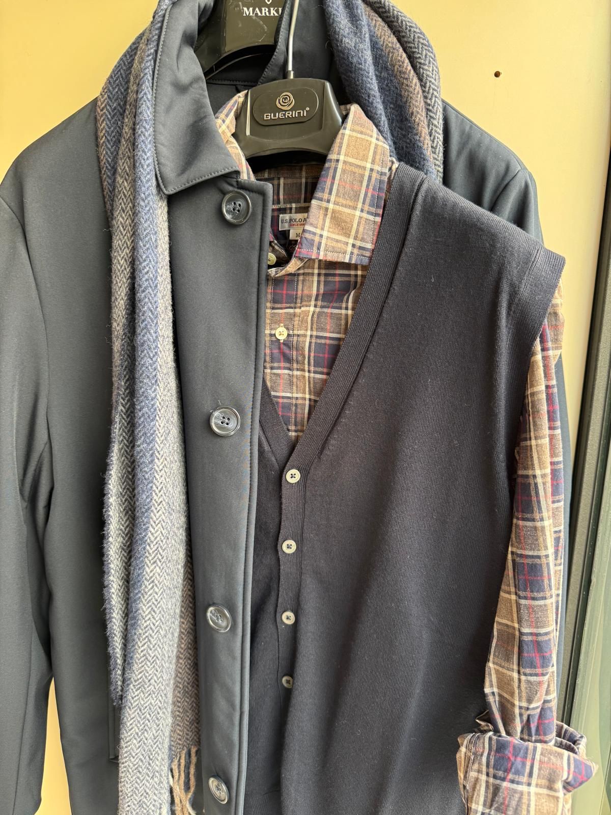 Cappotto blu navy, sciarpa, gilet e camicia a quadri disposti su una gruccia.