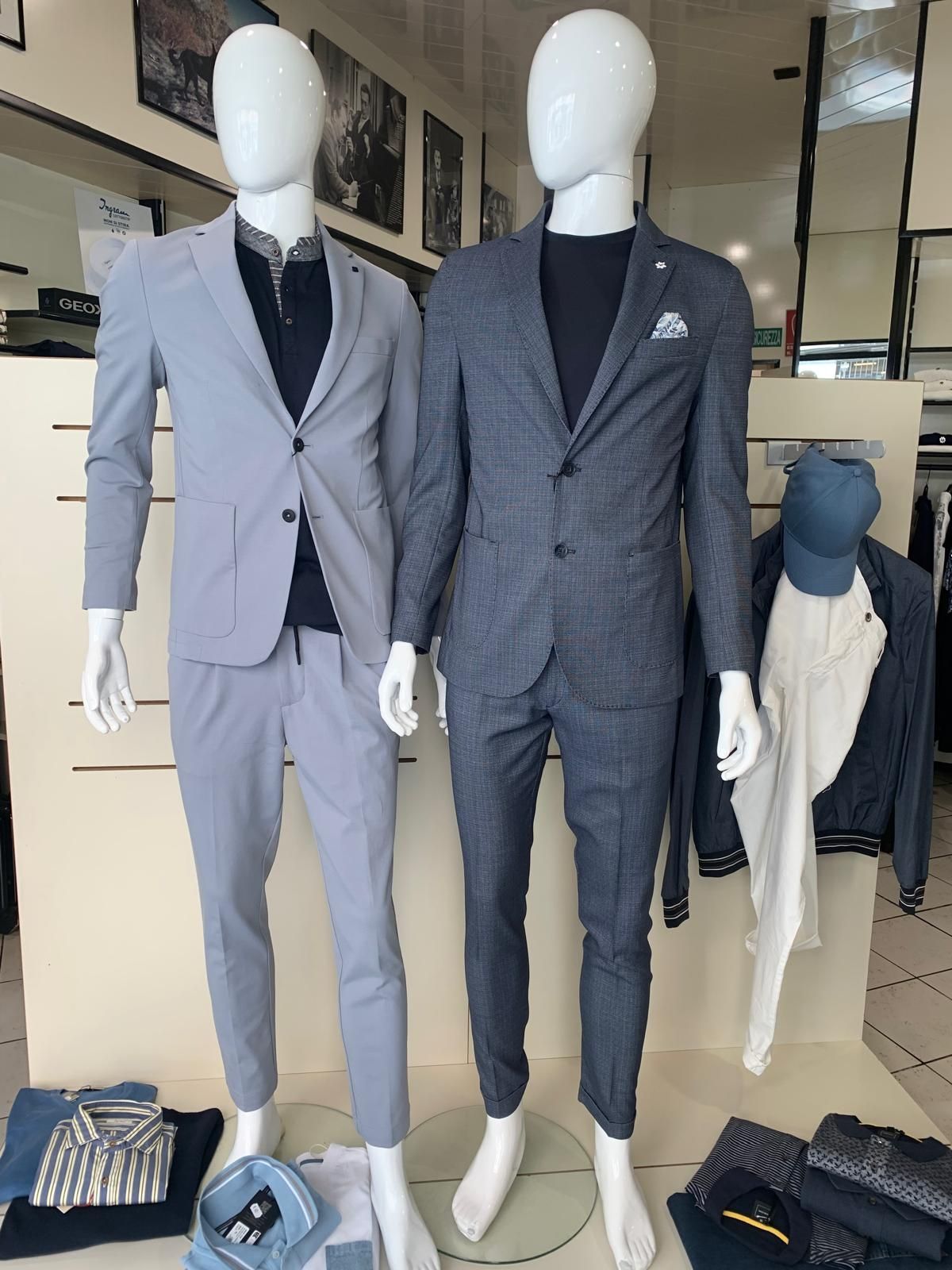 Manichino in un negozio che indossa un cappotto grigio sopra un gilet nero e un maglione con cappuccio; un altro manichino è sulla sinistra.