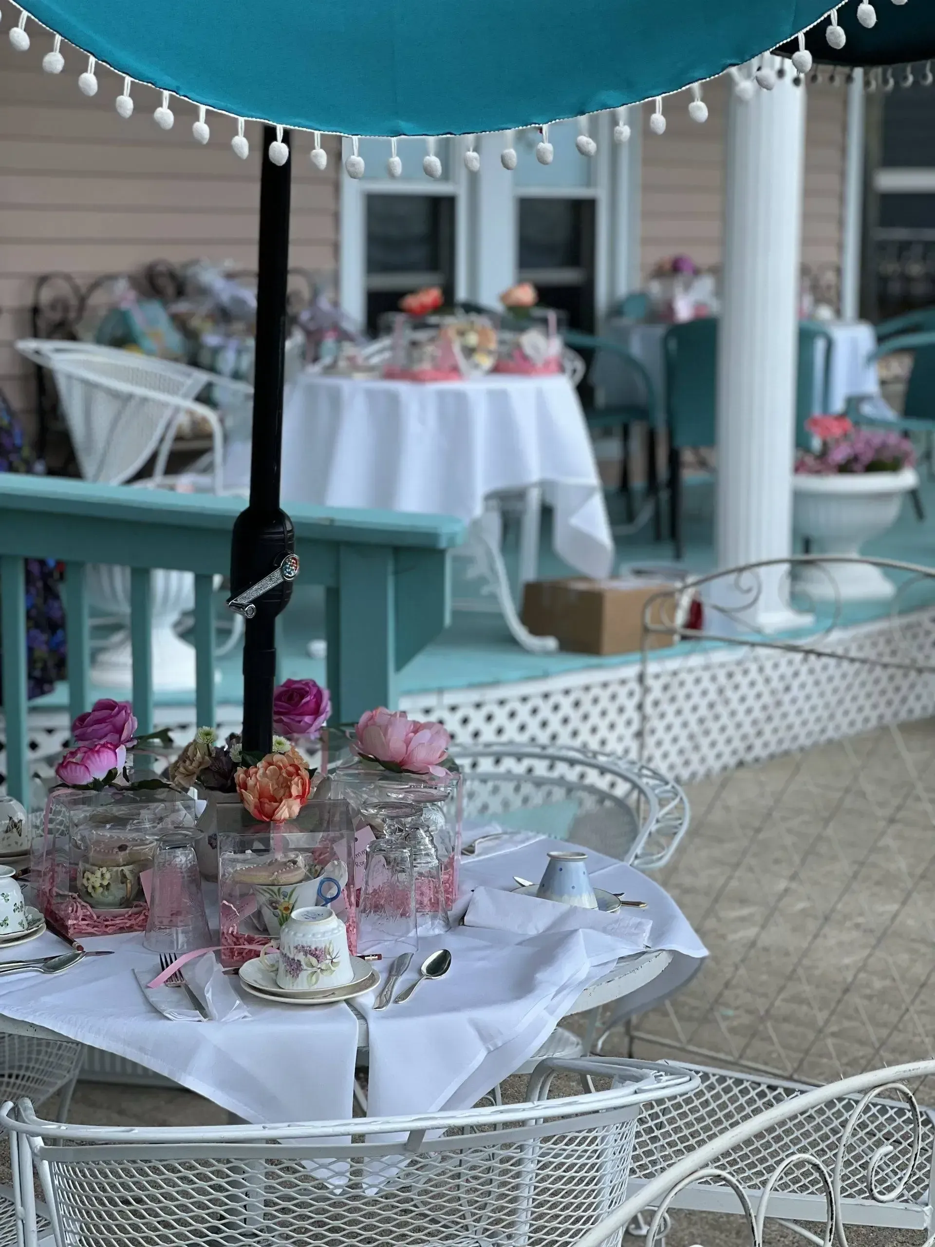 A table set up for a tea party on a porch under an umbrella.
