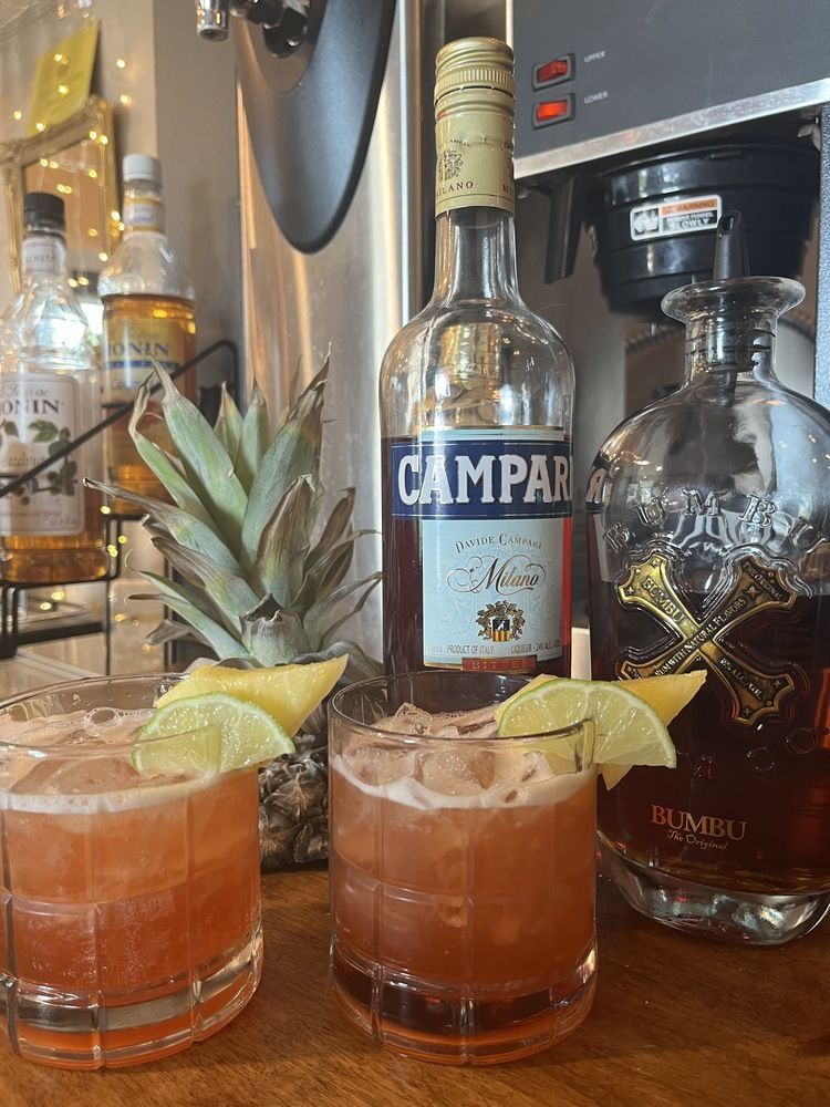A bottle of campari is sitting next to two glasses of cocktails.