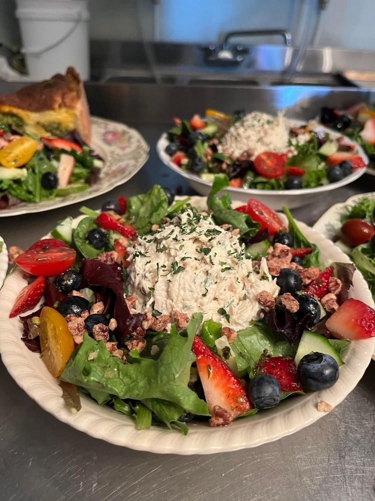 A paper plate topped with a salad and fruit on a table.