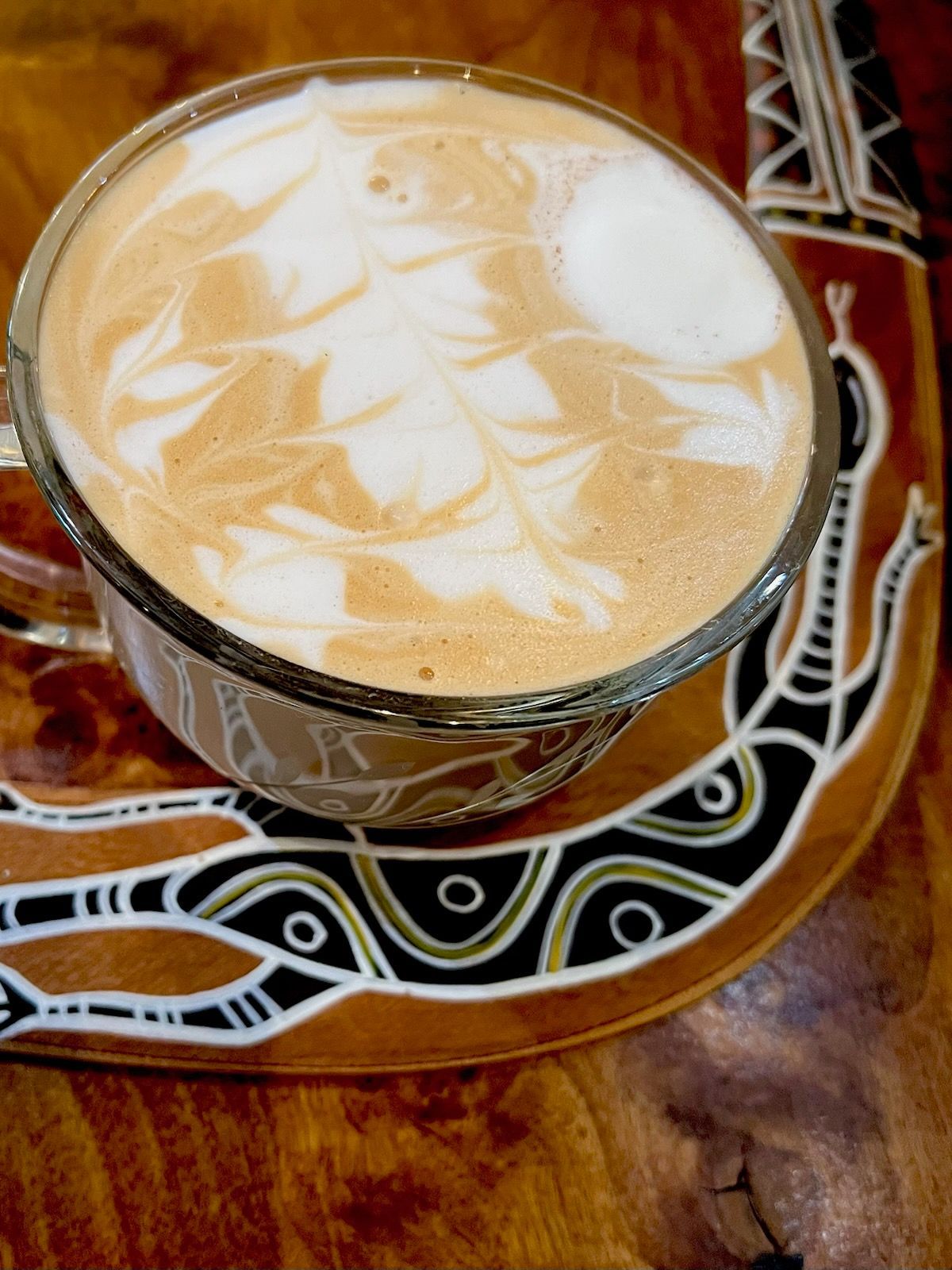 A cup of coffee sits on a saucer on a wooden table.