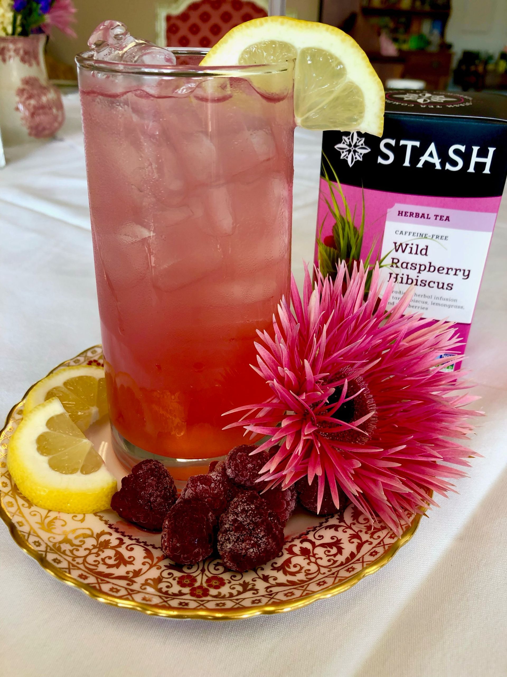A glass of raspberry tea with lemon slices on a plate.