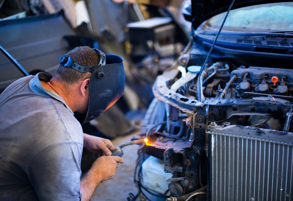 A Man Wearing a Welding Mask is Working on a Car in a Garage — Febos Welding and Engineering In Corrimal, NSW