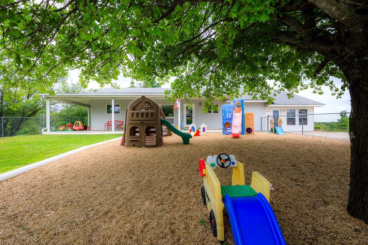 A playground with a slide and a house under a tree