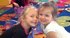 Two little girls are sitting next to each other on a rug.