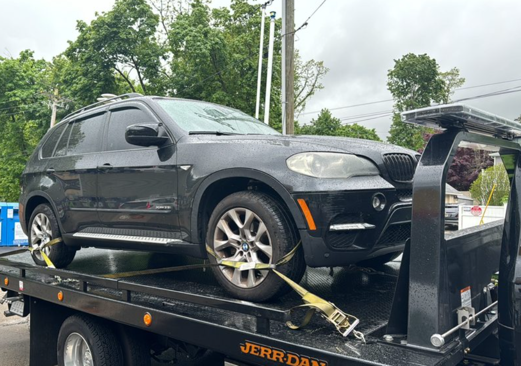 Black car being towed by a black tow truck; car is strapped down.