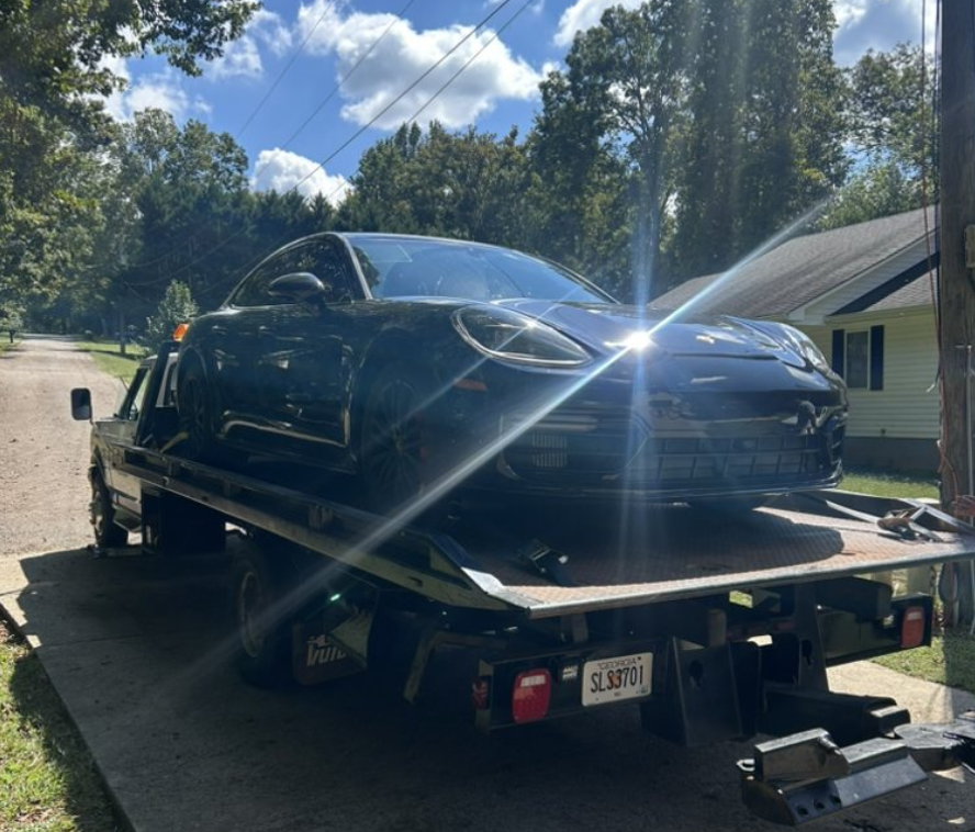 Green tow truck carrying a black car on a city street.