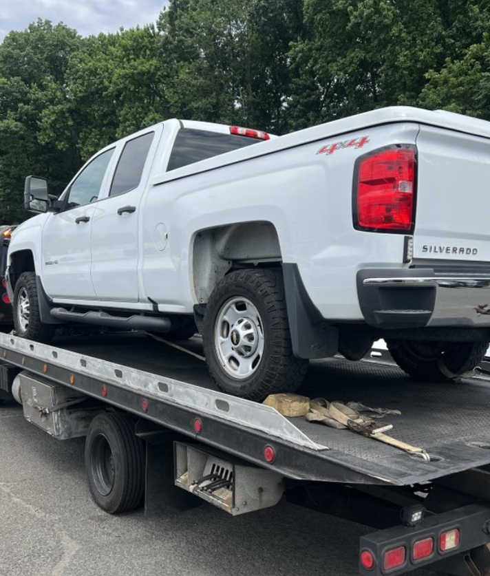 Black car being towed on a flatbed tow truck on a road with green grass.