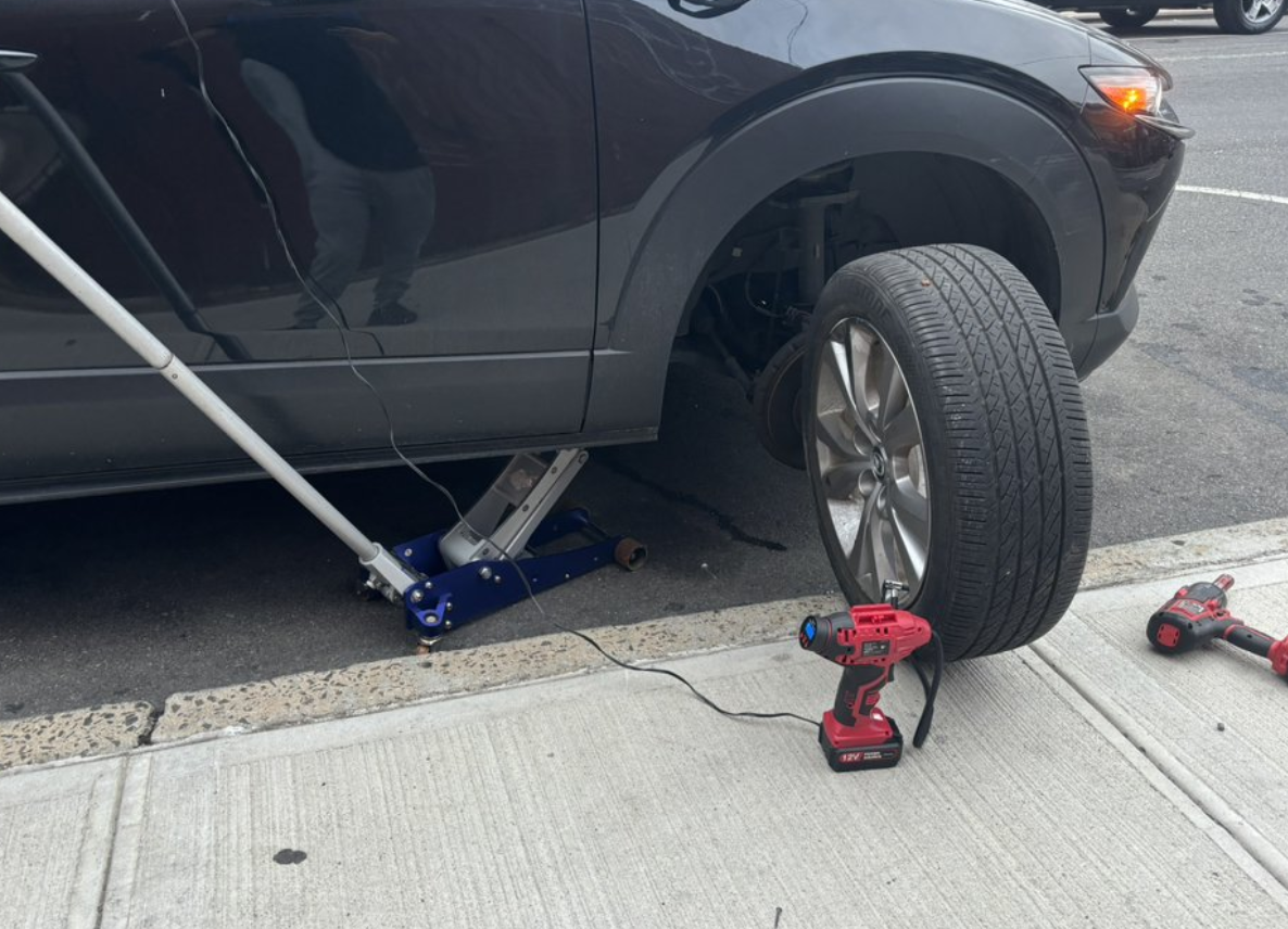 A black car getting a tire change on the side of the road.