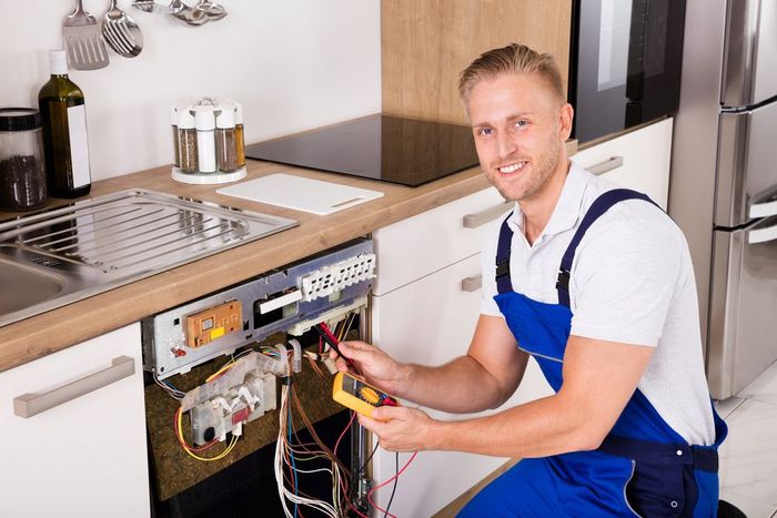 A man is working on a dishwasher in a kitchen.