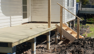 Newly built wooden deck and stairs attached to a white house; dirt pile in the foreground.