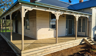 Wooden veranda of a house, newly built with natural wood, cream-colored siding, and green trim.