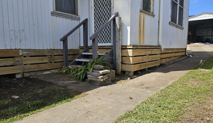 Exterior of a white house with wooden steps and a new wooden foundation. A concrete path leads alongside.