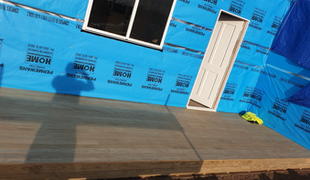 Construction site exterior: blue tarp, gray deck, white door and window, partially built.