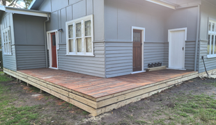 Wooden deck extension on a gray house, with a brown door, windows, and green grass.