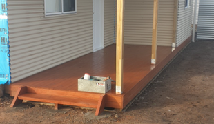 Wooden deck extension with brown stain, supported by posts, and a small step.
