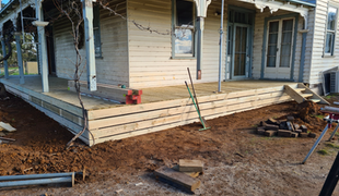 Wooden porch under construction next to a house with exposed ground and construction tools.