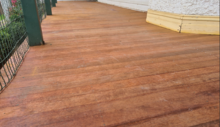 Wooden deck boards, reddish-brown color, running horizontally. Green support post and railing in the background.