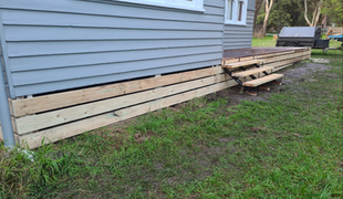 Grey house with wooden deck and steps on a grassy area.