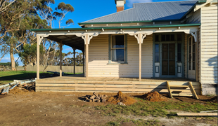Wooden house with porch and corrugated iron roof, deck under construction, sunny day.