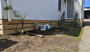 Wooden skirting around a white building's base. Soil, grass, and a door visible.