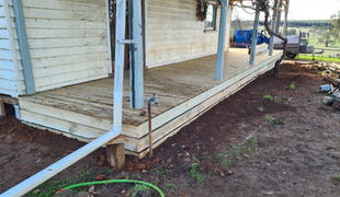 Wooden porch of a house with peeling paint and weathered boards; dirt and grass in the foreground.