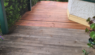Wooden deck half-cleaned, showing the contrast between weathered gray and fresh red-brown color.