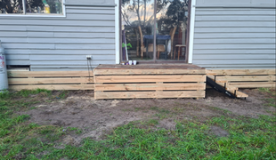 Wooden steps and landing outside a house with sliding glass doors.  Green grass and gray siding visible.
