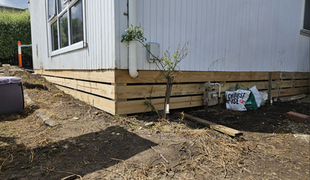 Wooden skirting around the base of a white building, brown earth in the foreground.