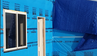 Exterior wall with window, door, and blue weather barrier.