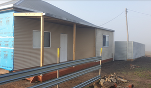 Exterior of a tan building under construction with a black roof, a metal storage unit, and foggy setting.