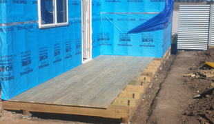 Wooden deck under construction with blue house wrap and a window.