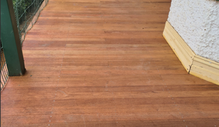 Wooden deck with horizontal planks, next to a stucco wall with yellow trim.