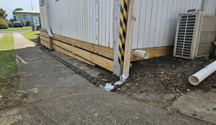 Building with wooden base, concrete path, and gutter downspout.