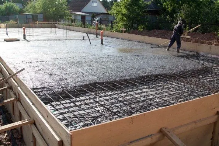 Worker leveling fresh concrete over rebar mesh foundation.